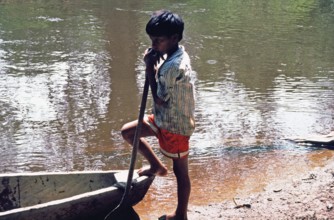 Little boy standing next to a boat, Rio Yanayacu, Amazon region near Iquitos, Peru, South America,
