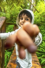 Young child pointing forward while exploring a lush rainforest trail on a wooden walkway,