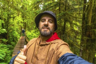 Happy tourist gesturing thumbs up while taking a selfie on a wooden walkway through a lush