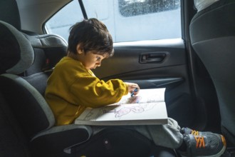 Young child is sitting in a car seat, happily drawing with crayons in a coloring book during a road
