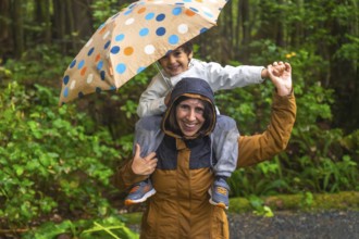 Happy mother giving piggyback ride to her smiling son under an umbrella while walking in a