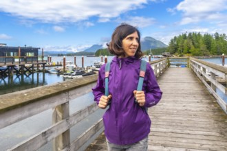 Female tourist wearing a purple jacket and carrying a backpack walking along a wooden pier in