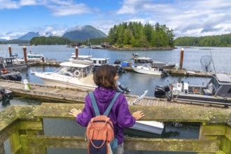 Female tourist with backpack contemplating moored boats in tofino harbor, vancouver island, british
