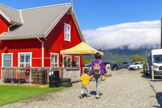 Mother and her young child are walking away from a vibrant red building in tofino, vancouver