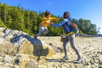 Joyful child leaping from a rock into mother's outstretched arms on a sunny tofino beach,
