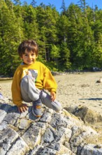 Young boy sitting on a large rock at a beach in tofino, british columbia, soaking up the summer sun