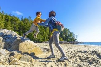 Mother catching her son as he joyfully jumps from a rock on a sandy beach, surrounded by lush green
