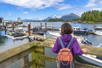 Young woman with a backpack enjoying the scenic view of boats in tofino harbor on a sunny summer