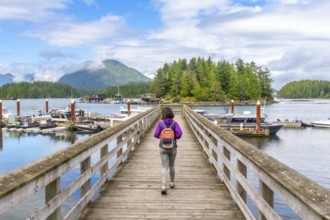 Female tourist with backpack walking down a wooden pier in tofino, british columbia, with boats,