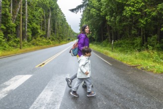 Mother and son crossing a paved road through lush rainforest in ucluelet, vancouver island,