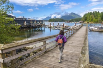 Female tourist with backpack walking down a wooden pier in tofino, british columbia, canada,