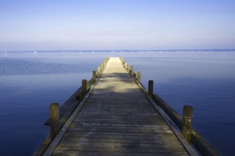 A long wooden walkway leads into the still water of a huge lake under a clear sky, Steinhude