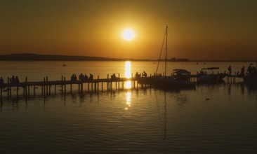 Sunset over the Steinhuder Meer with people on a pier, reflecting sailboats, peaceful, Steinhude