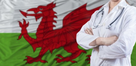 Doctor with crossed arms on Wales flag. Welsh health and care concept. Female doctor on Wales flag