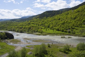 A quiet river surrounded by green hills and trees under a partly cloudy blue sky, Kvabliani River