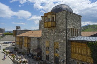 Buildings with stone walls, decorative wooden elements and domed roof under a blue sky, Rabati
