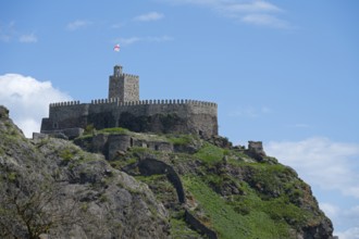 Medieval castle on a steep hill with stone walls and a watchtower under a blue sky, Rabati