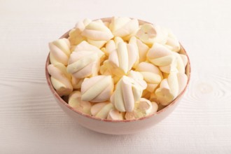 Orange and pink marshmallow in ceramic bowl on white wooden background, side view, copy space,