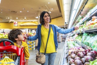 Mother points to fresh vegetables while shopping with her son in the produce section of a grocery