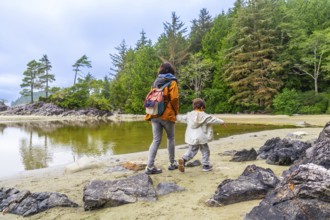 Mother and son walking along the shore of mackenzie beach in tofino, enjoying the breathtaking