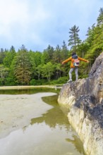 Female hiker standing on rock with open arms, enjoying the serene view of the inlet and lush forest