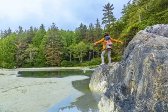 Tourist with open arms is standing on a rock enjoying the beautiful scenery of a beach in tofino. A