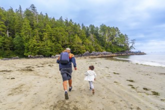 Father and son are running on a pristine sandy beach with lush green forest in the background,