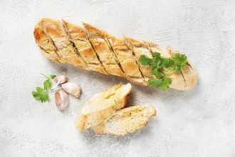 Garlic bread, baguette with garlic butter and herbs, on a light table, top view