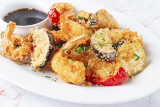 Shrimp and assorted vegetables are deep fried in a light batter and served on a white plate. A