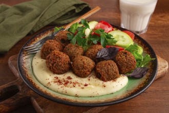 A plate holds falafel balls, tahini, salad with tomatoes and cucumbers, and a drink. The setting is