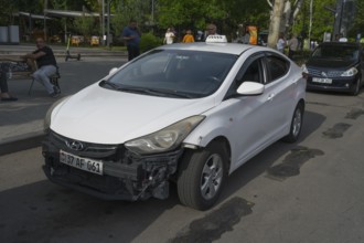 White Hyundai with frontal damage on the side of the road, people in the background, Armenia
