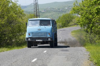 A blue truck drives on a winding country road through green hills, MAZ trucks, exhaust gases,
