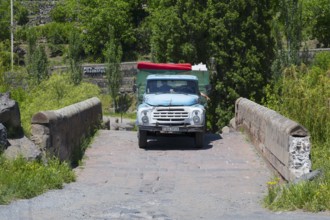 A blue truck drives over an old stone bridge surrounded by trees, truck ZIL-130 drives over Kassagh