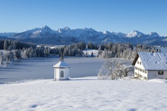 Snowy landscape with chapel, farm and mountains in the background under clear sky, Hegratsrieder