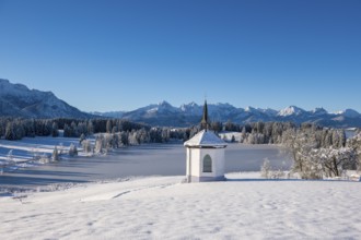 Snowy landscape with chapel and mountains in the background under clear blue sky, Hegratsrieder
