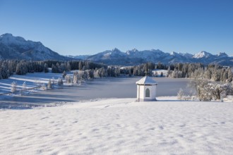Snow-covered plain with a chapel and mountains under bright blue sky, Hegratsrieder See, near