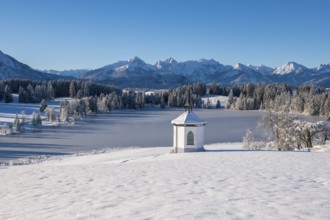 Landscape with snowy chapel on the shore of a frozen lake in front of Bergen, Hegratsrieder See,