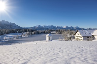 Snowy landscape with chapel, farmhouse and mountains under brilliant sunshine, Hegratsrieder See,