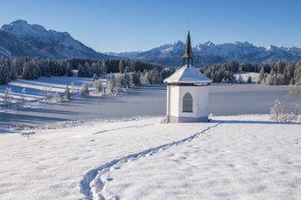 Small chapel in winter with footprints in the snow and mountains in the background, Hegratsrieder