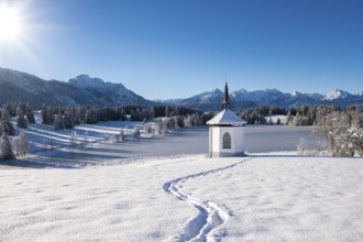 Chapel in snow with footprints and sunny mountain landscape, Hegratsrieder See, near Füssen,
