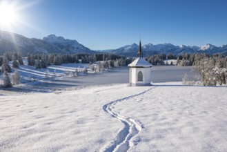 Snowy landscape with chapel and footprints, surrounded by mountains and forests, Hegratsrieder See,