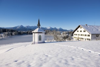 Chapel and farmhouse in snowy landscape with mountains in the background, clear atmosphere,