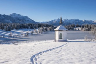 Snowy landscape with chapel and footprints against a mountain backdrop, Hegratsrieder See, near