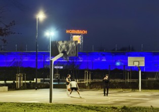 Men on Ernst-Kuzorra-Platz in front of the royal blue Glückauf battle track in the evening,