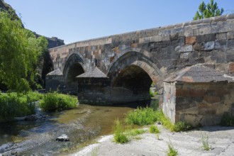 Old stone bridge with several arches across a small river surrounded by lush nature and green