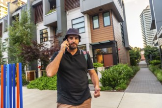 Bearded male tourist wearing bucket hat and backpack is using his smartphone while walking near