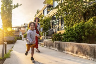 Happy child running joyfully on the sidewalk in vancouver, british columbia, canada, with mother