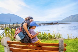 Mother and her son are sitting on a bench, enjoying the scenic view of shuswap lake and the public