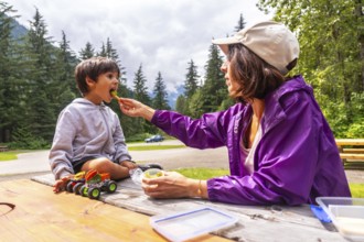 Mother feeds her son a healthy snack at a picnic table in hemlock grove, a beautiful boardwalk in