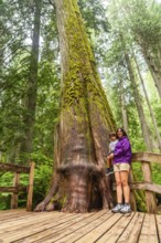 Mother holds her child while standing on a wooden boardwalk, marveling at a massive, moss covered